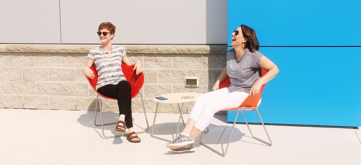 Two women sitting outside a building in orange chairs