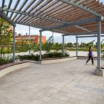 Woman walks under an arbor with wall mounted wood benches surrounding