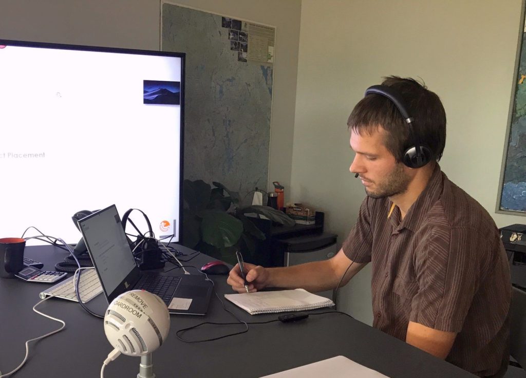Man wearing headphones looking at a laptop beside a presentation screen