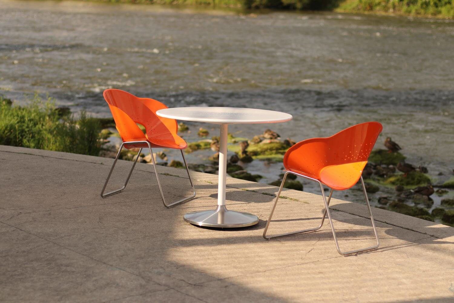 HOME_INSTALLATIONS_TABLES & SEATING_Maglin Photoshoot_Battery Table & Chairs Orange chair with a white circular table overlooking a river