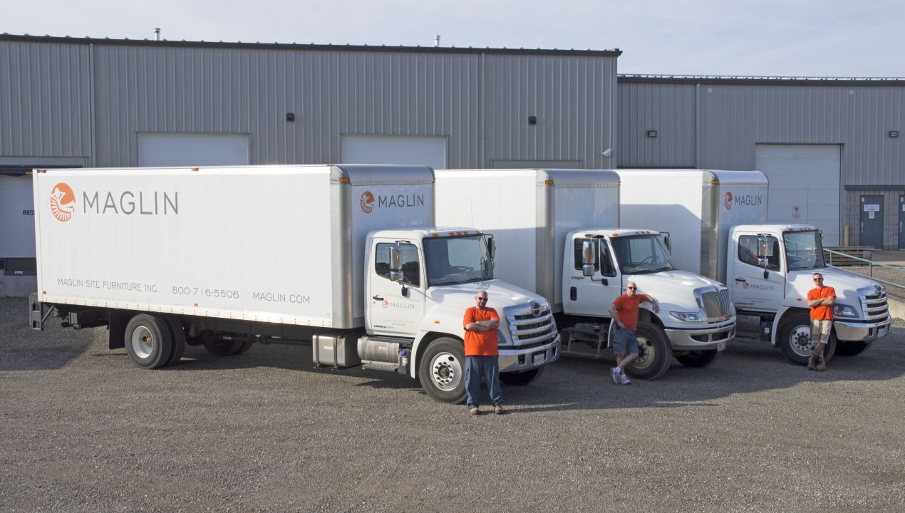 Maglin branded delivery trucks lined up with drivers standing in front