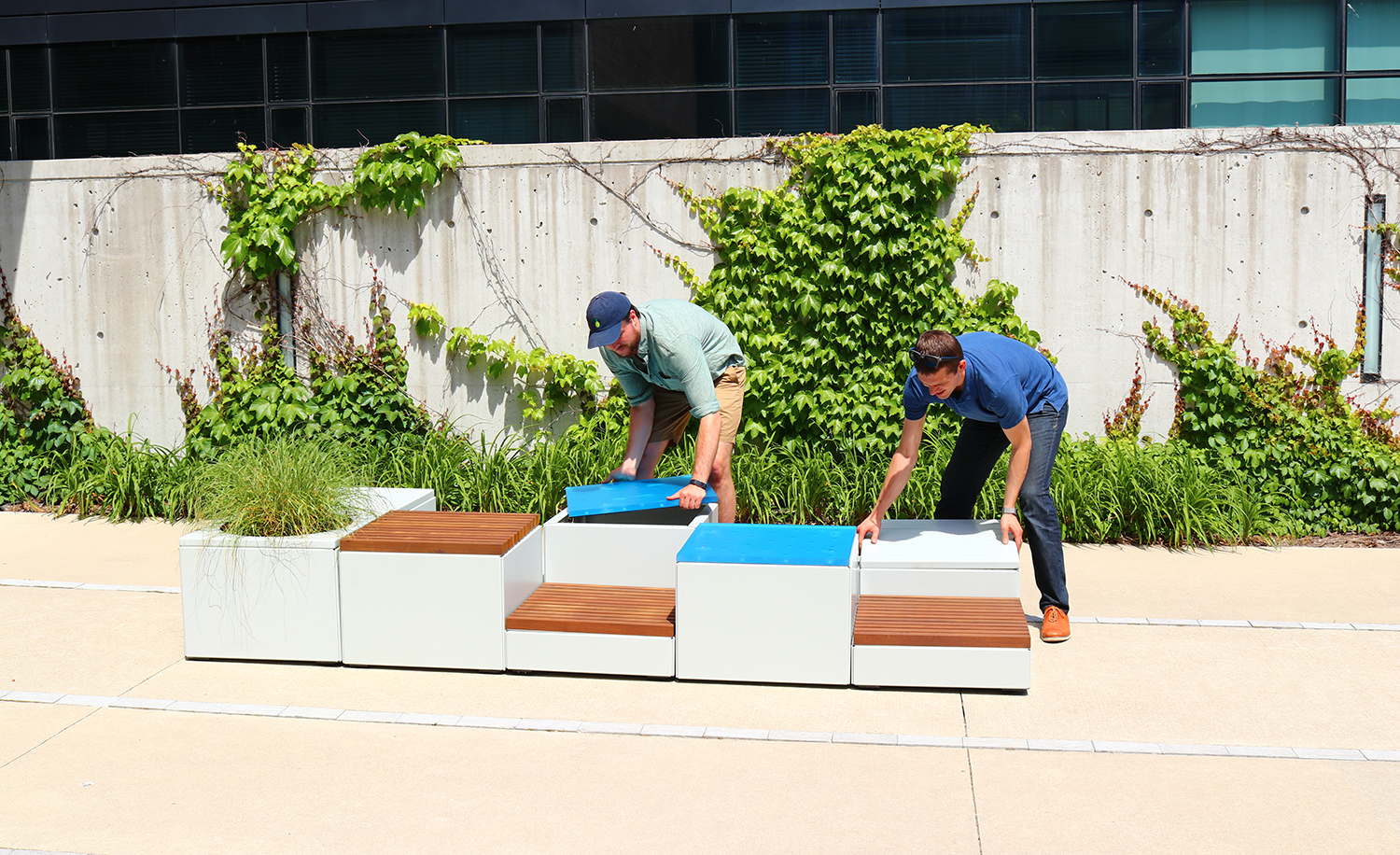 Two men assembling Pixel blocks against a wall with greenery