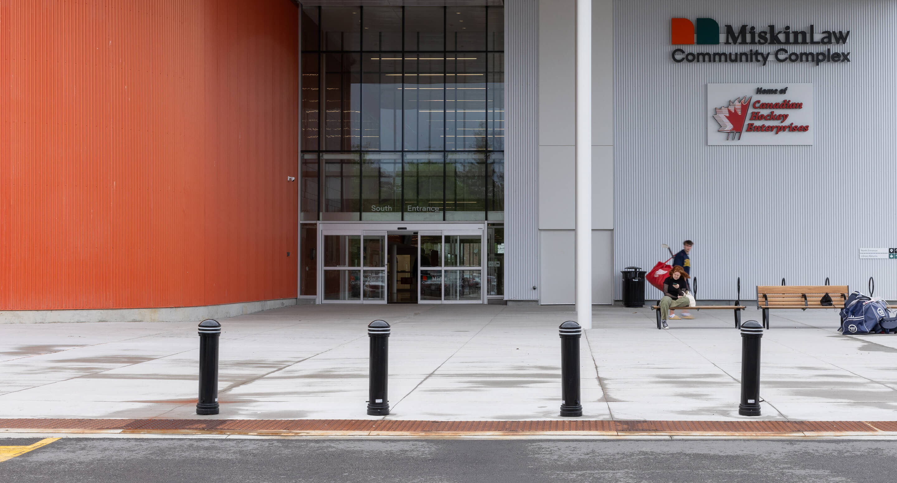 A person with hockey equipment walks toward the entrance of the Miskin Law Community Complex, home of Canadian Hockey Enterprises, drawing inspiration from its renowned installations and sporting legacy.