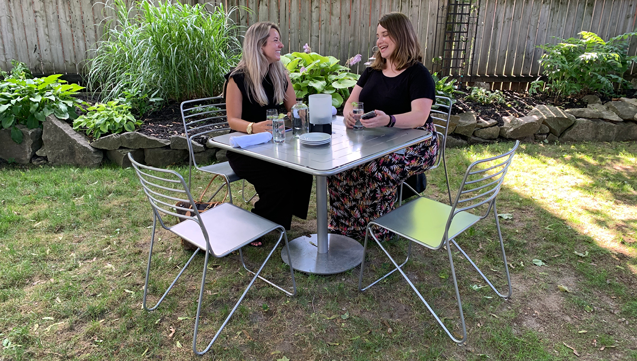 Two women sitting at metal Patio table in a backyard setting