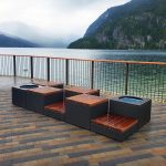 Bench with wooden seating and built-in planters on a tiled terrace overlooking a lake and forested mountains on a cloudy day.