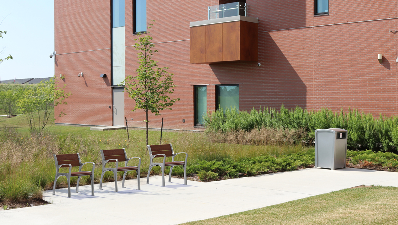 870 Chair in Ipe Wood with greenery next to brick building and 1400 recycle container