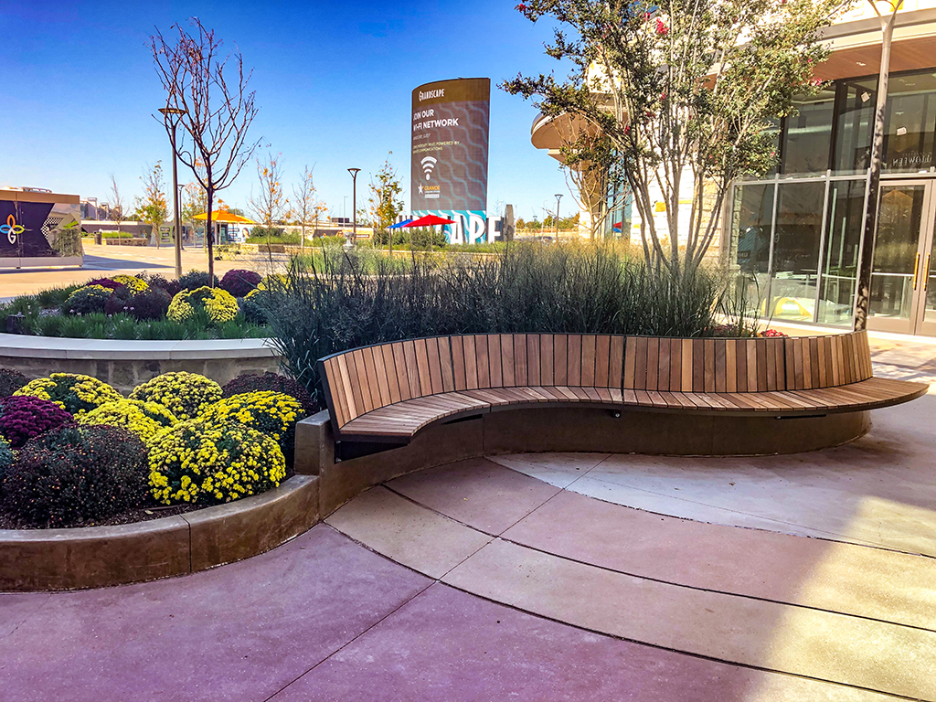 Grandscape_Ogden_Wide Shot_Entrance Wood Ogden curved bench attached by cantilever mount to concrete wall next to flower beds