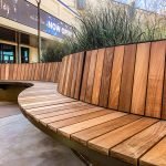 Closeup of a curved section of a wood Ogden Bench with a building entrance in the background