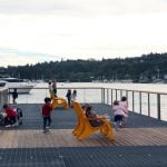 Children sit on yellow lounge chairs on a pier overlooking a waterway