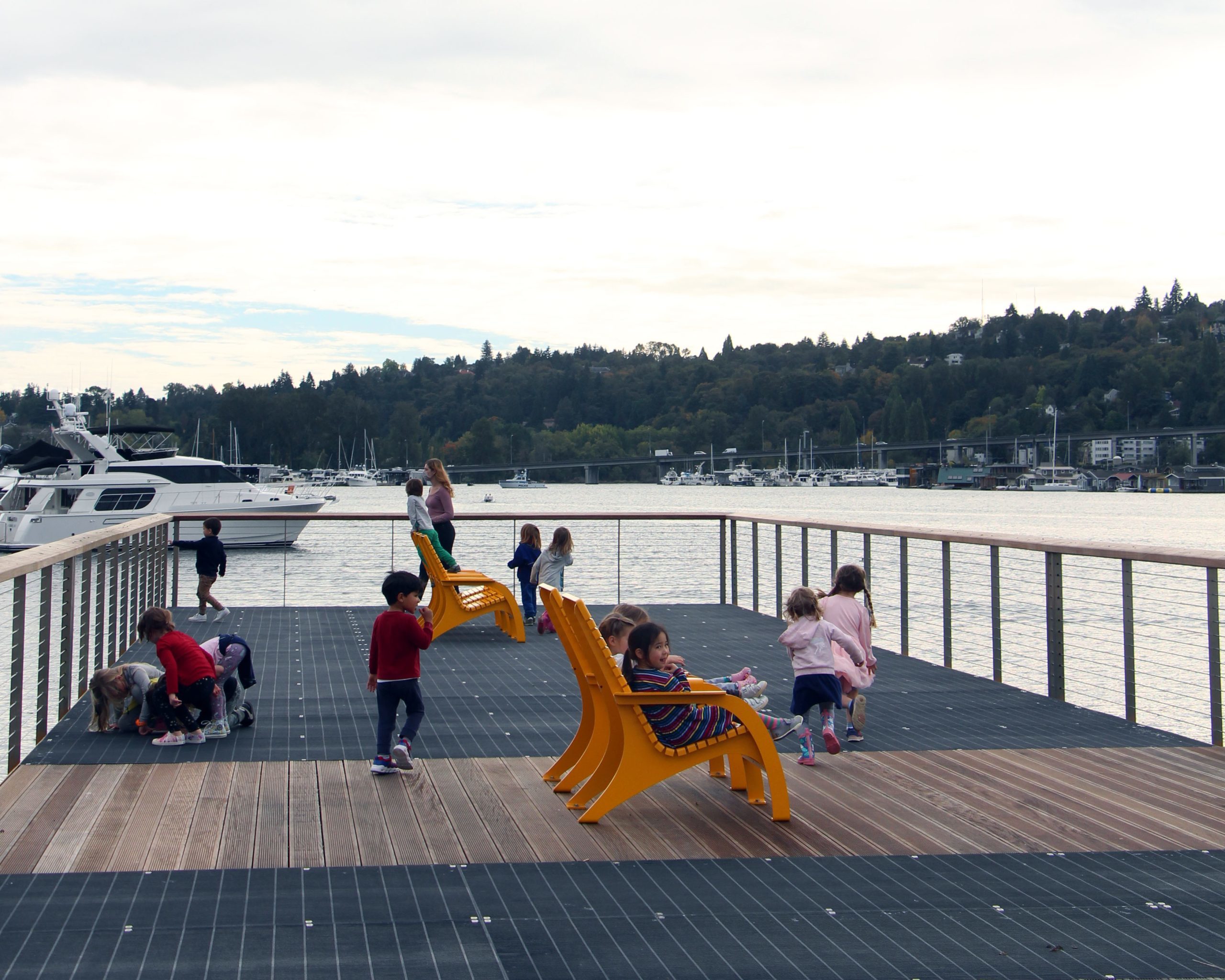 Children sit on yellow lounge chairs on a pier overlooking a waterway