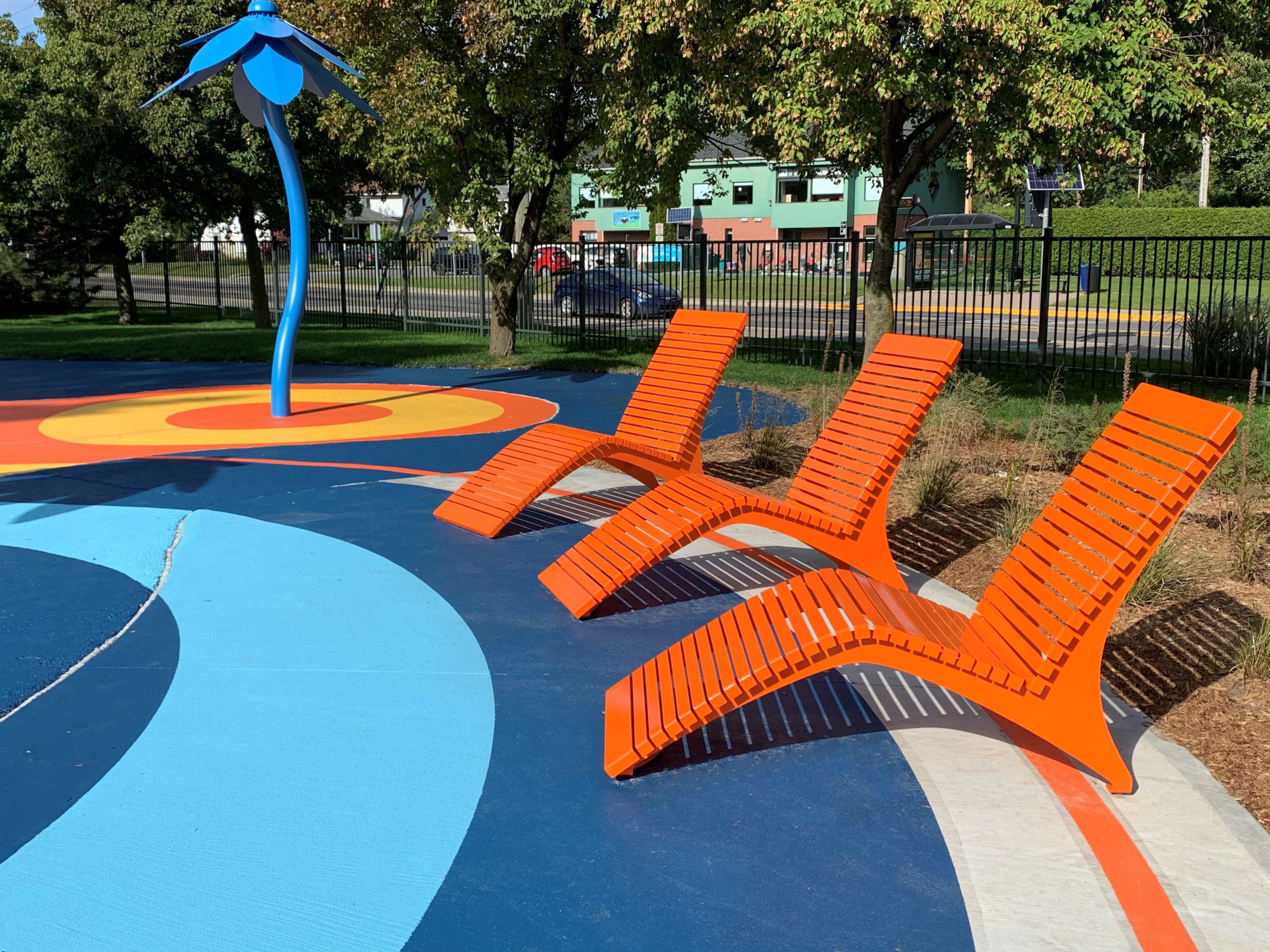 Three Orange 720 Lounge Chairs face a splash pad in a park.