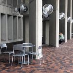 Three sets of Foro tables and chairs are show next to a concrete building.