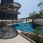 Lasercut cloud-shaped canopy structure casts a dappled shadow next to children playing at the Battery Playscape