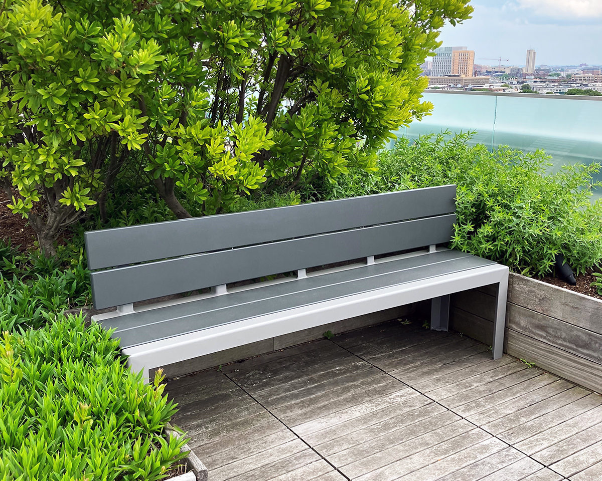 A Backed 1050 Bench is nestled between raised wooden planters on the roof deck of Viridian Apartments.