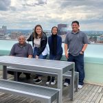 Four maintenance workers at the Viridian Apartments smile pose on the roof deck with newly installed 1050 tables and benches. The Boston skyline is in the background.