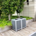 Two side-by-side 1050 Waste & Recycling containers in front of a raised planting bed with grasses and trees on the rooftop deck of the Viridian Apartments in Boston.