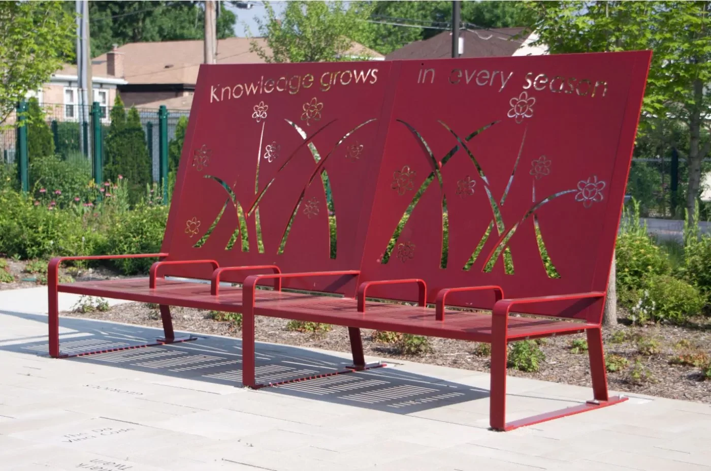 A red metal bench with floral cutouts and the phrase 