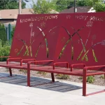 A red metal bench with floral cutouts and the phrase 