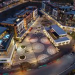 A drone image of the AGORA mixed use development at night. Seating is underlit by LEDs and circular spotlights light up the square.