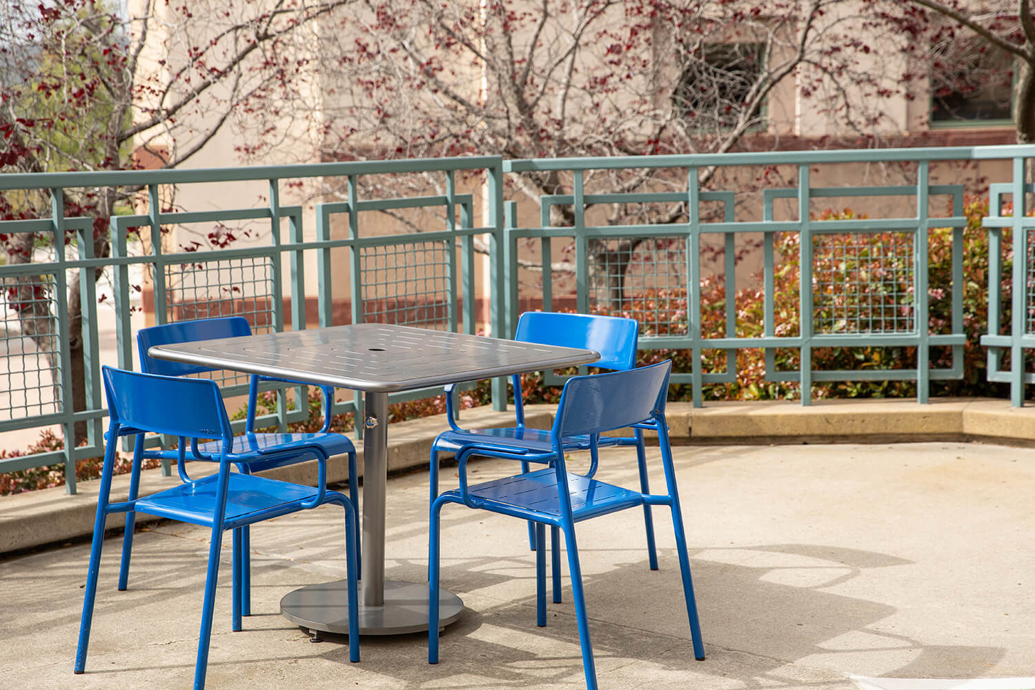 Maglin Foro tables and chairs painted blue and silver at CSUSM patio surrounded by lush gardens