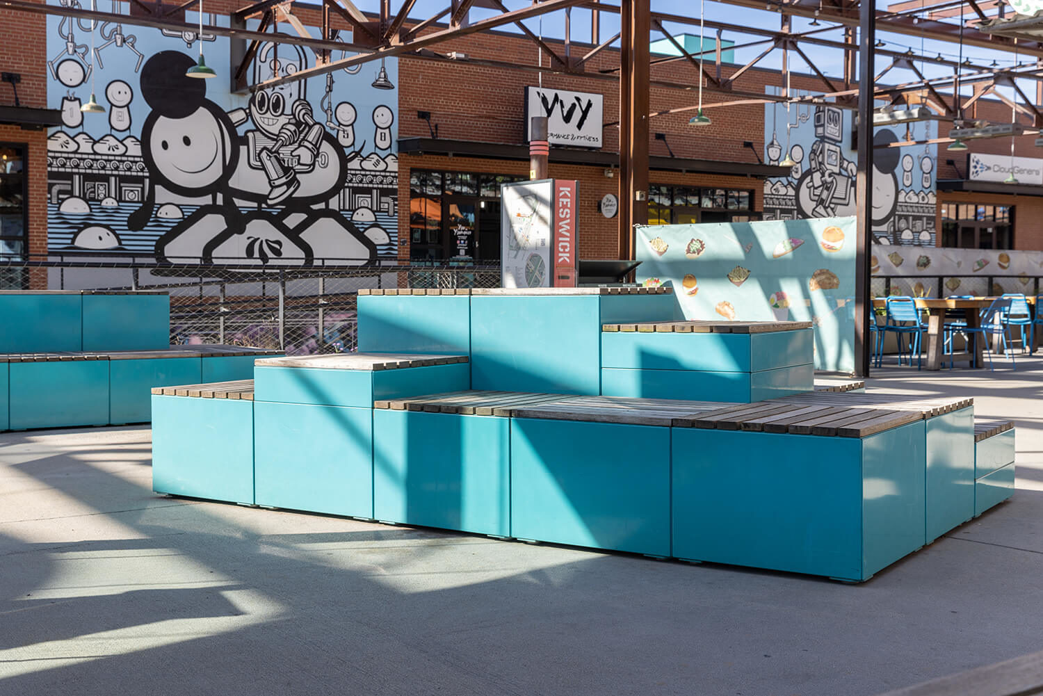 Turquoise painted Maglin Pixel Blocks are stacked on a patio with robot murale in background at Camp North End