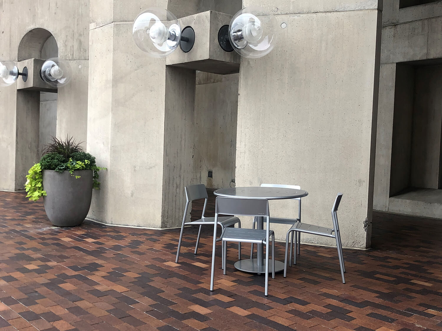 Foro Maglin tables and seating next to concrete wall with giant bulb lighting and planter