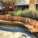 Curved Ogden bench cantilevered to a concrete ledge with gardens and buildings in background