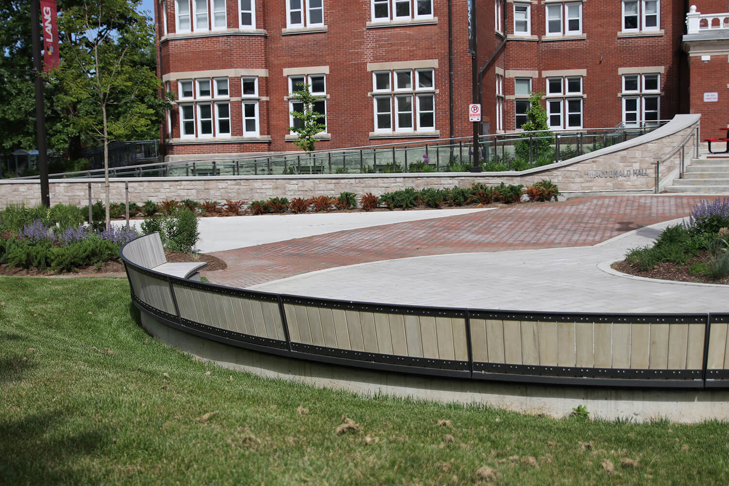 Long curved Ogden bench facing red building a Macdonald Hall, Lang Plaza