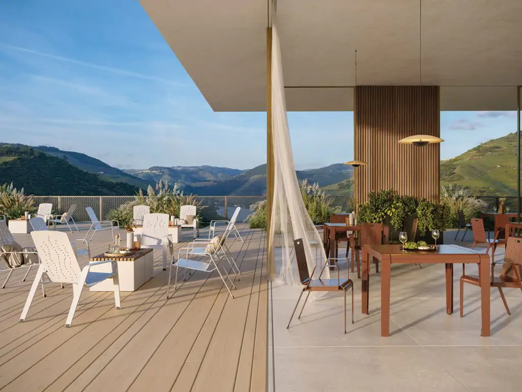 Modern outdoor patio with lounge chairs, tables, and mountain views. One side features wooden deck seating; the other has dining tables and a sheer curtain blowing in the breeze.