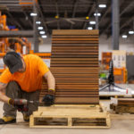 A Maglin employee wearing an orange t-shirt drills and assembles a 720 lounge chair in the warehouse.