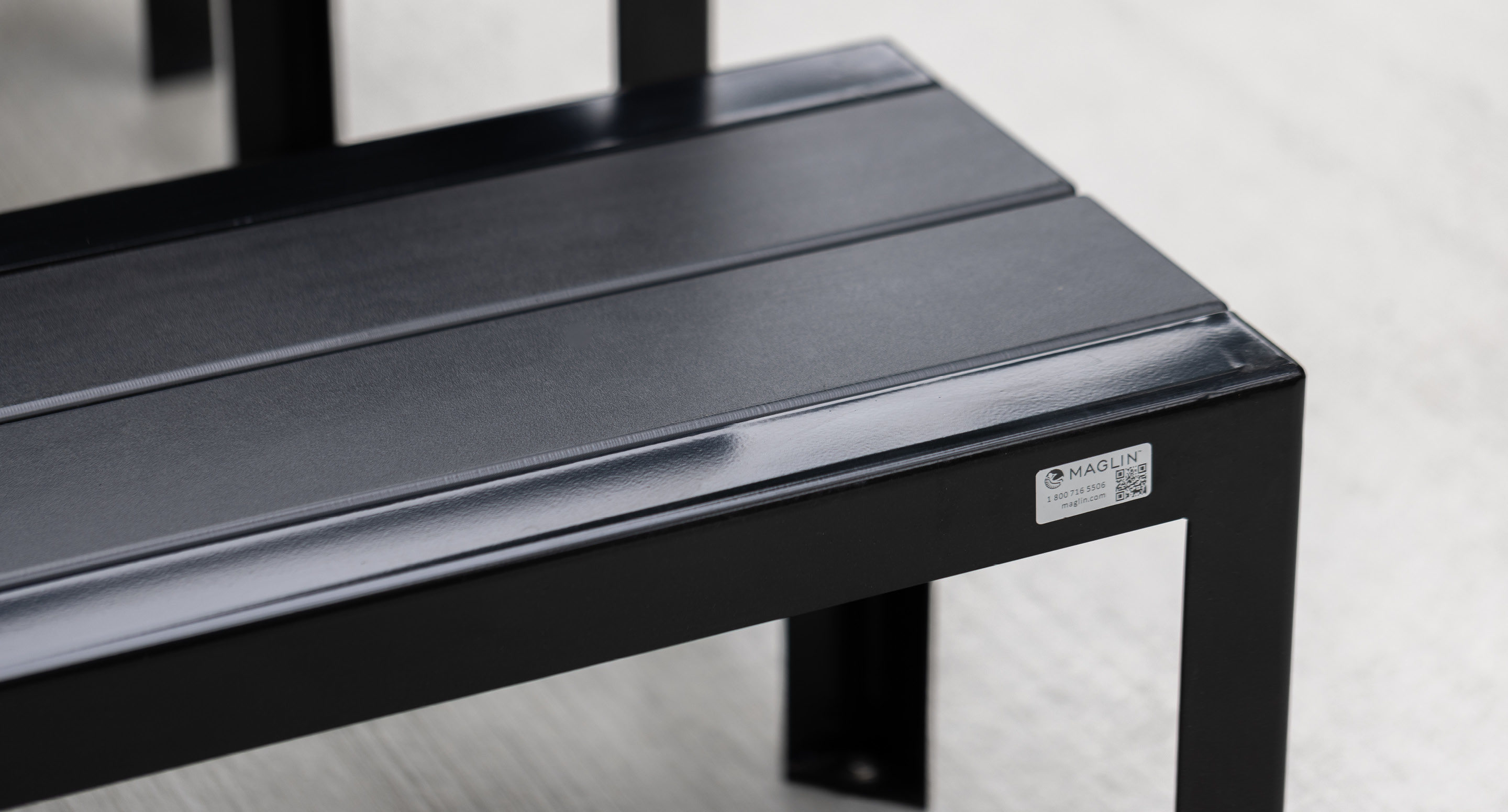 Close-up of a black metal bench with a small label on the side, positioned on a light-colored surface.