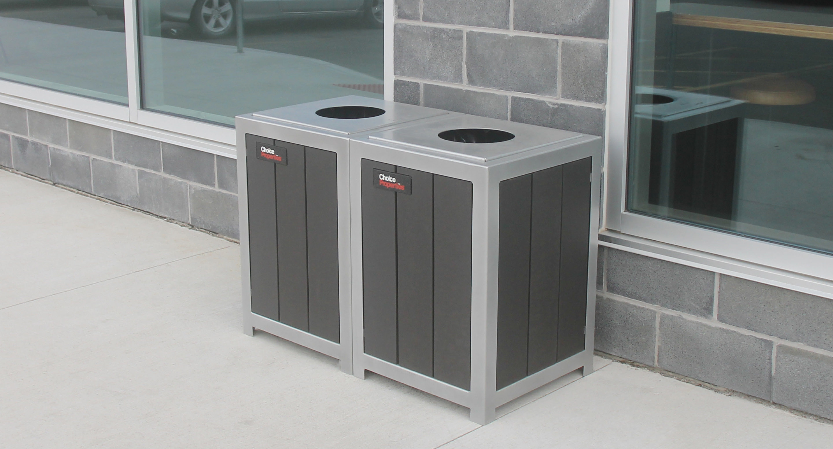 maglin-collections-1050-gallery8 Two rectangular outdoor trash bins with circular openings are placed side by side against a brick wall near a window.