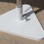 A close-up of a white triangular metal base supporting a vertical pole on a concrete surface.