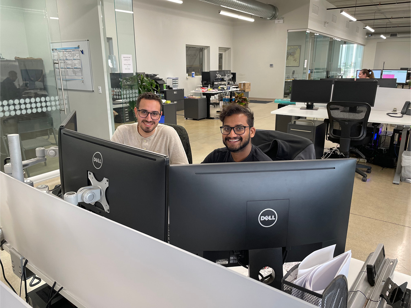 Two men sitting at computers in an office setting, smiling