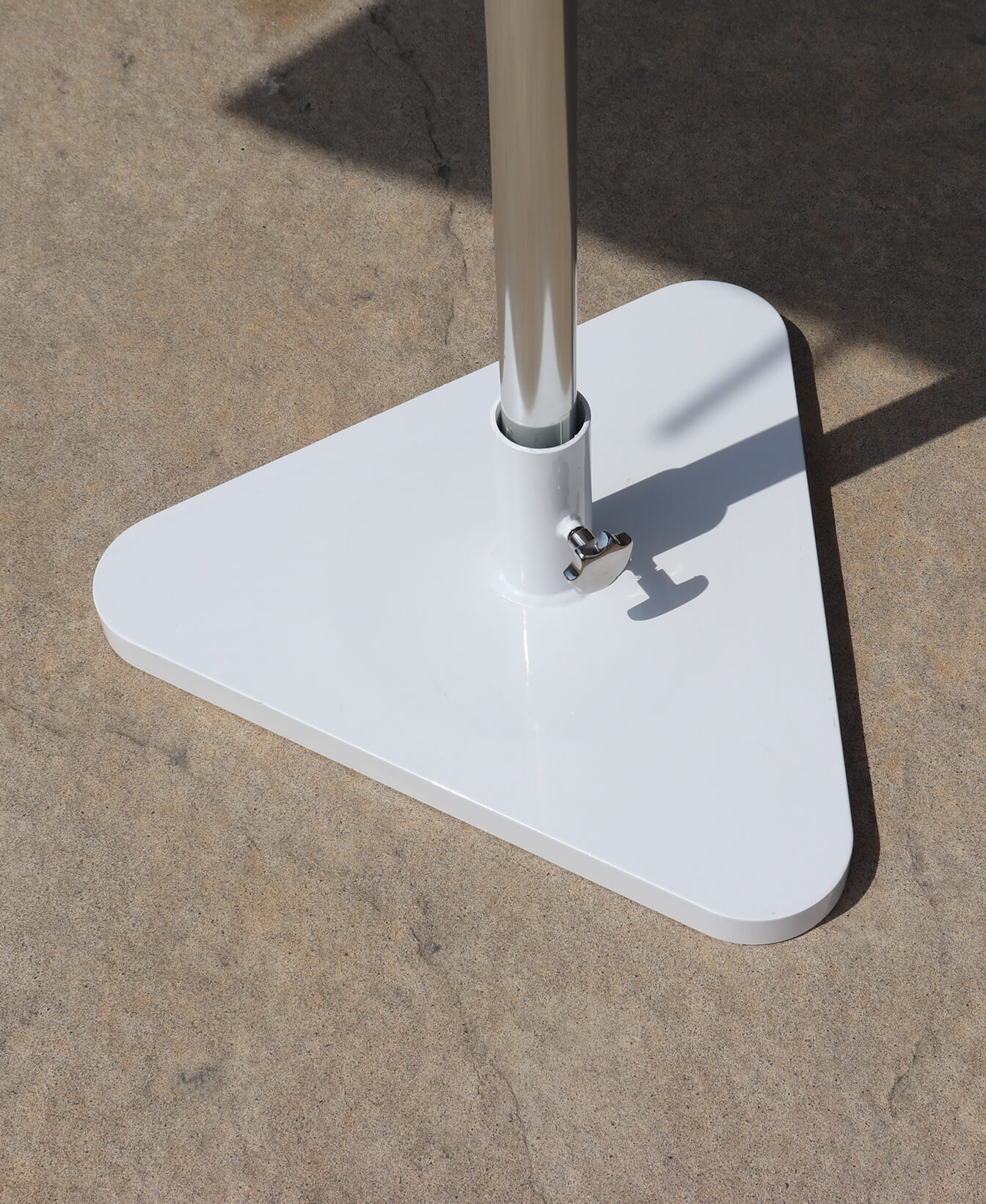 A close-up view of the Kontur Umbrella Base, a white, triangular metal base supporting a vertical pole on a concrete surface.