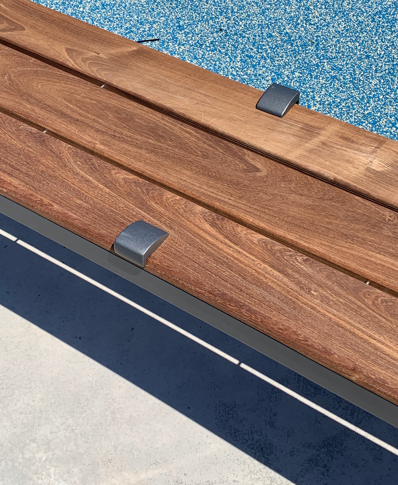 Gros plan sur le Dispositif anti-planches à roulettes 300 - monté sur un banc en bois avec des supports métalliques - sur une surface bleue mouchetée et un sol en béton.