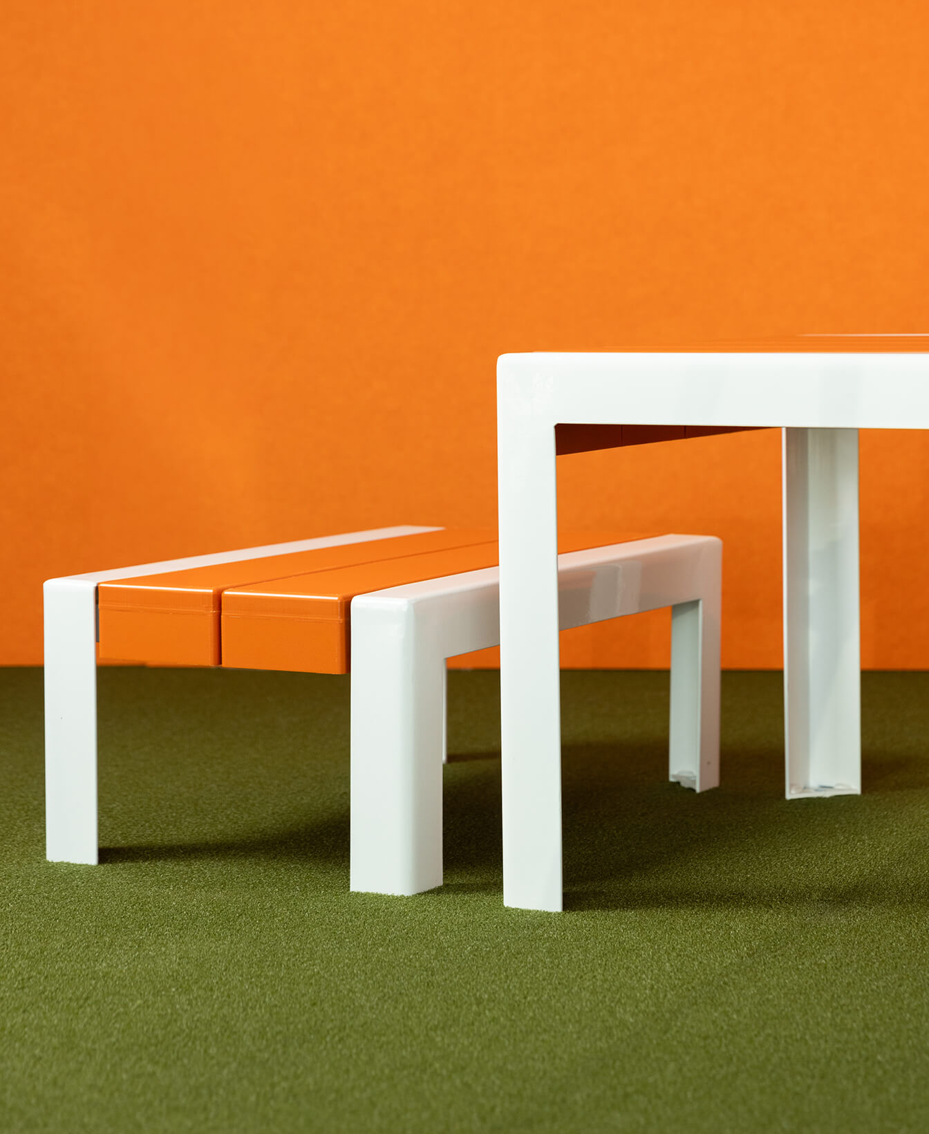 The 1050 Children's Bench with orange seats is paired with a white table, set on green carpet against an orange background.
