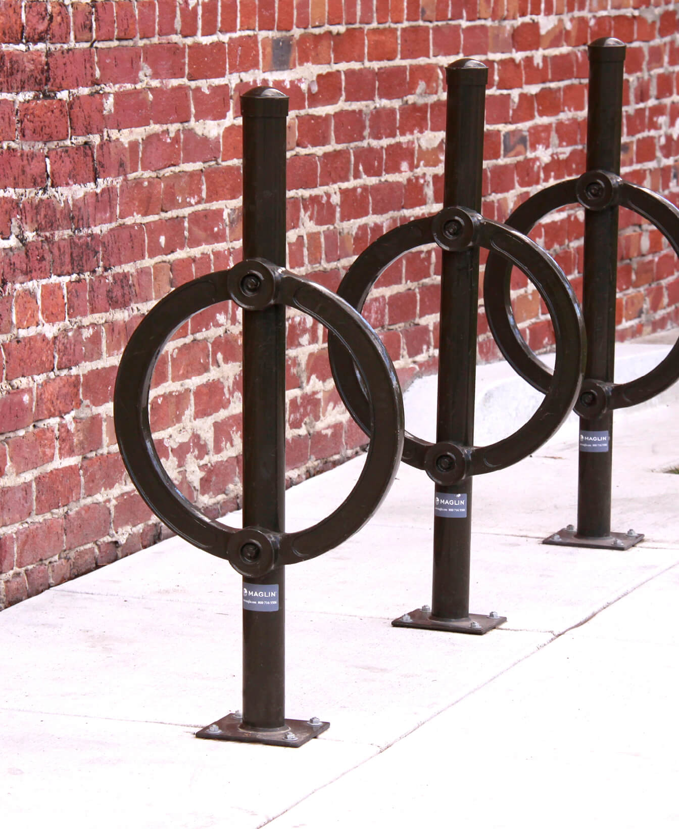 Une rangée de Support à vélos 200 supports à vélos en métal installés sur un trottoir à côté d'un mur en briques.