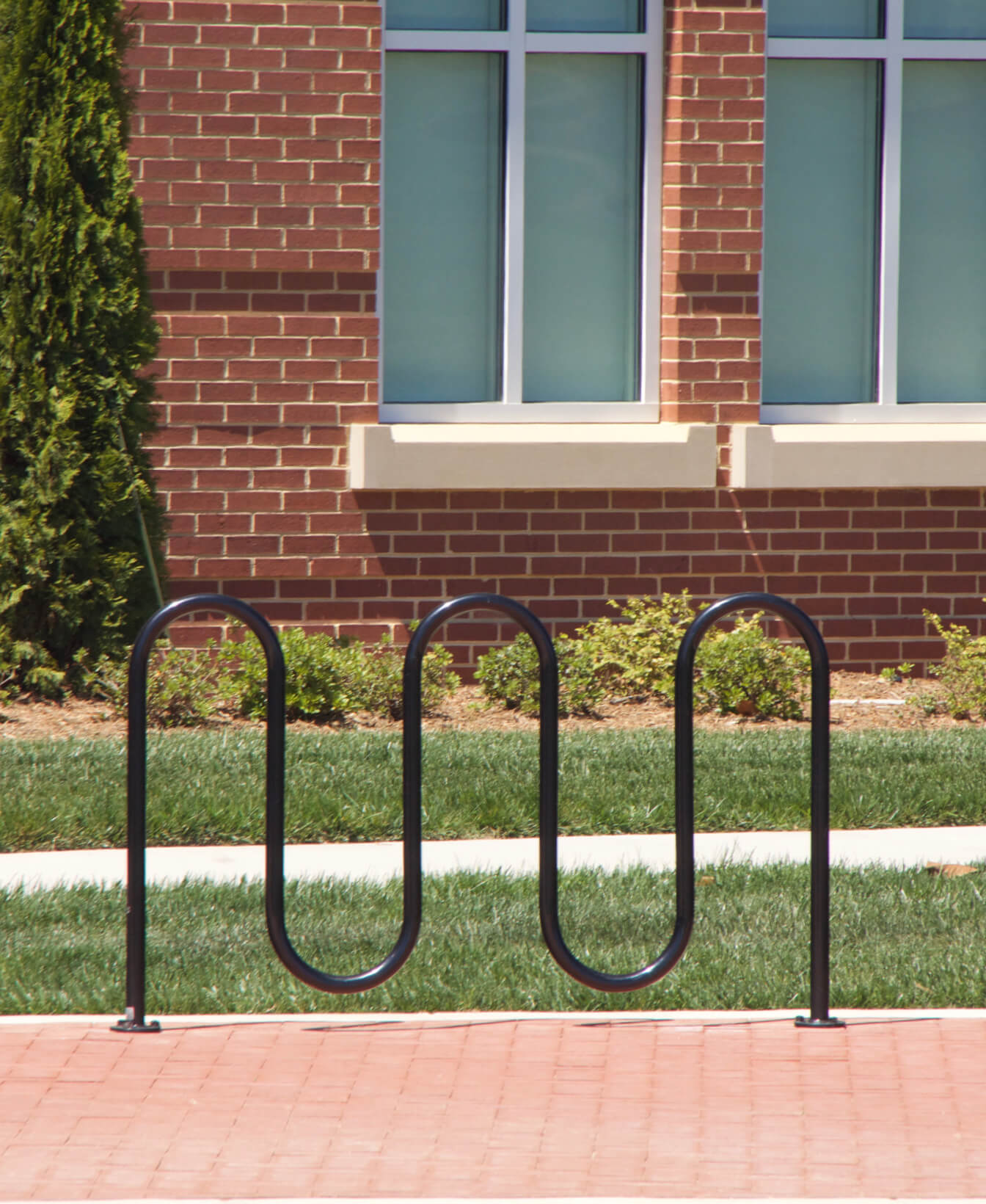 A 400 Bike Racks black metal bike rack is installed on a sidewalk in front of a brick building with windows and landscaping.