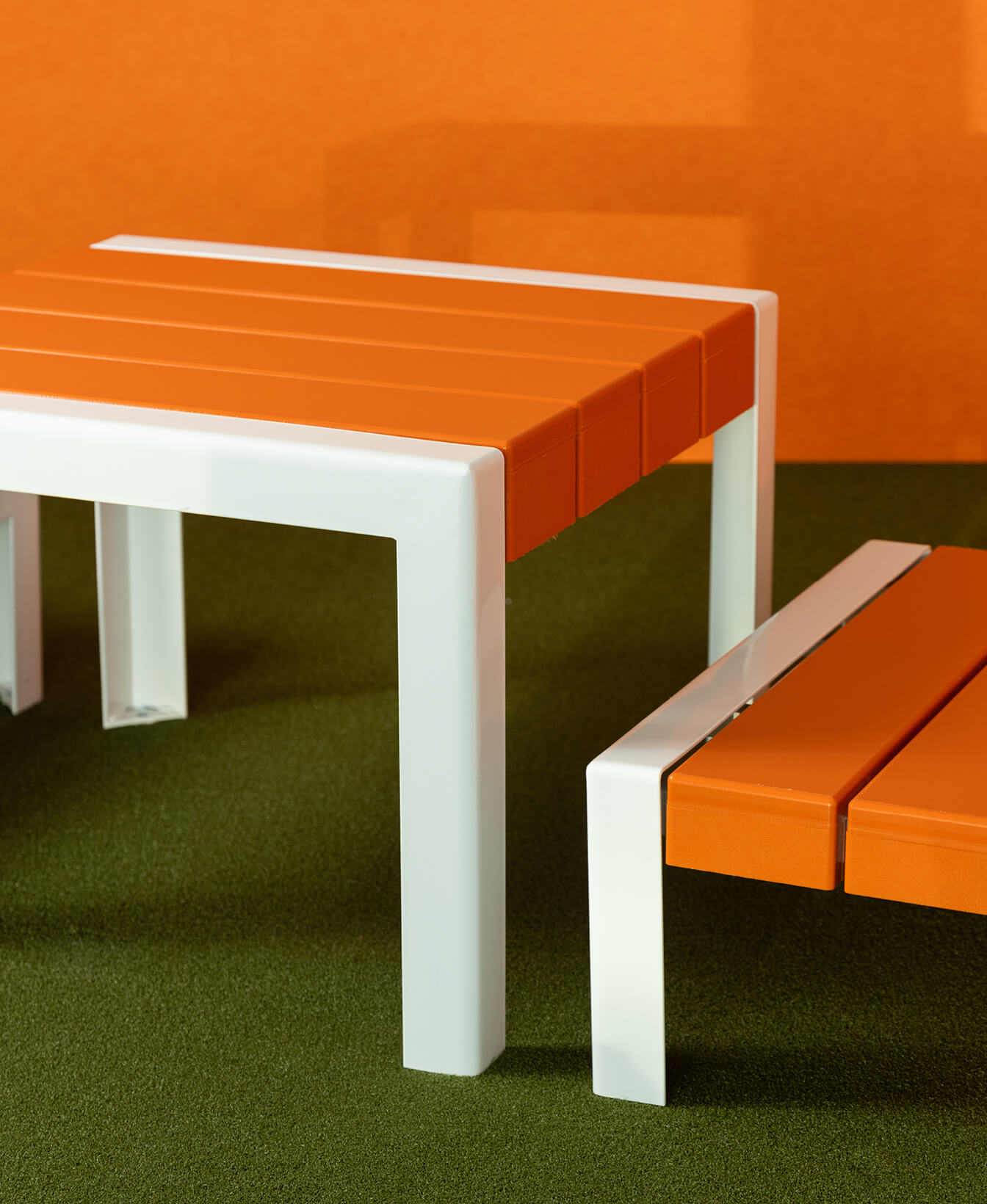 La Table 1050 pour enfants, avec ses lattes orange et ses pieds blancs, est posée sur une surface verte avec un fond orange.