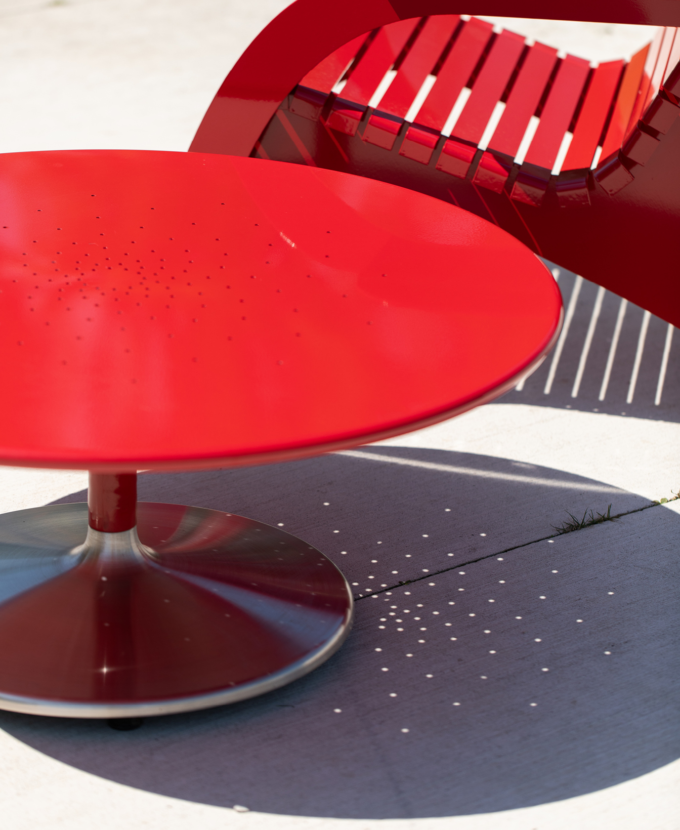 Battery Lounge Tables in bold red metal cast patterned shadows onto a sunny concrete surface, paired with a modern matching chair.