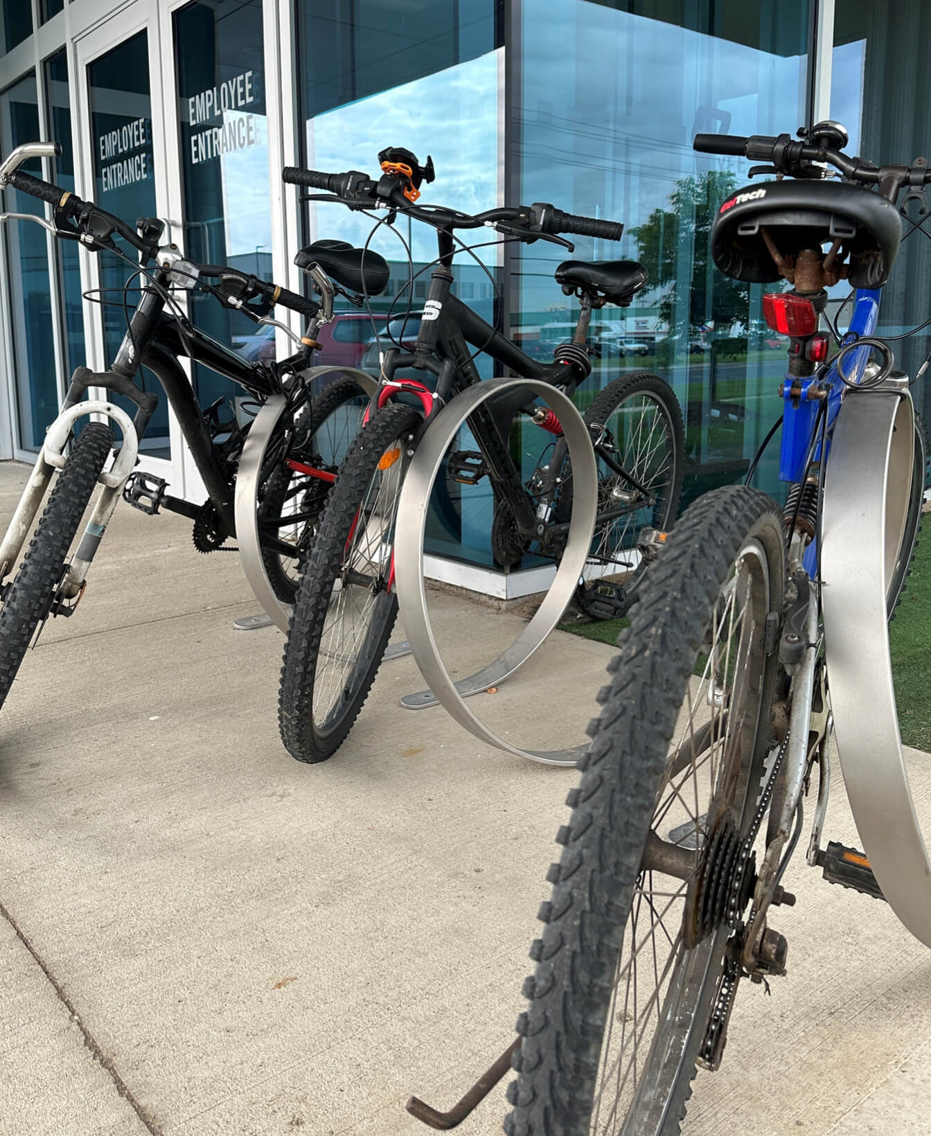 Four bicycles are parked in an Orbit Bike Rack outside a building with glass doors labeled "Employee Entrance.