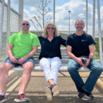 Maglin employees, Steve, Max, and Mike sit on a swing in front of Maglin pond.