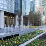 Immeuble de bureaux moderne avec une façade en verre, des parterres de fleurs aménagés, une fontaine et l'enseigne