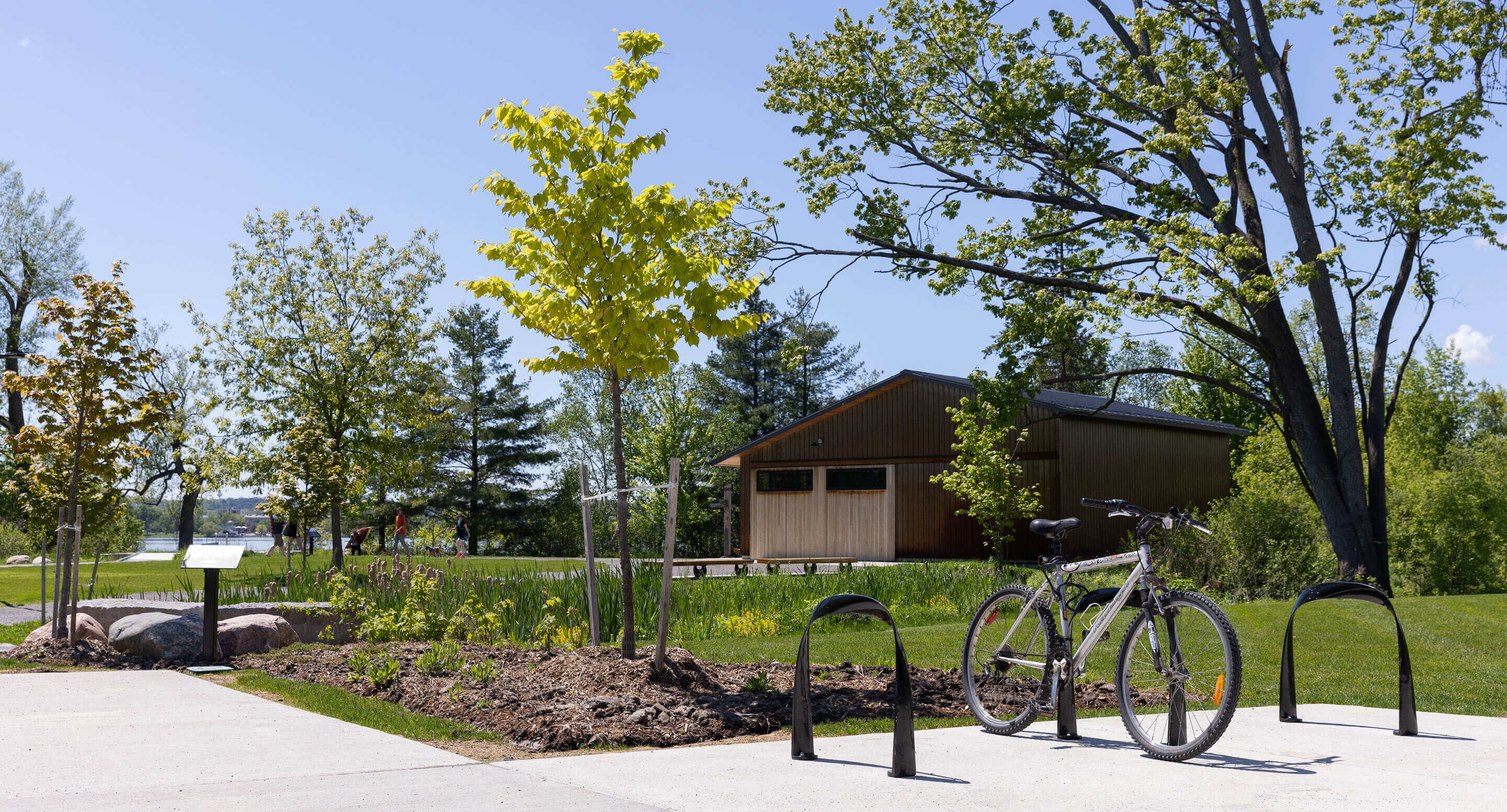 A bicycle is parked at a bike rack on a sunny day near the Canadian Canoe Museum, next to a wooden building surrounded by trees and green grass.