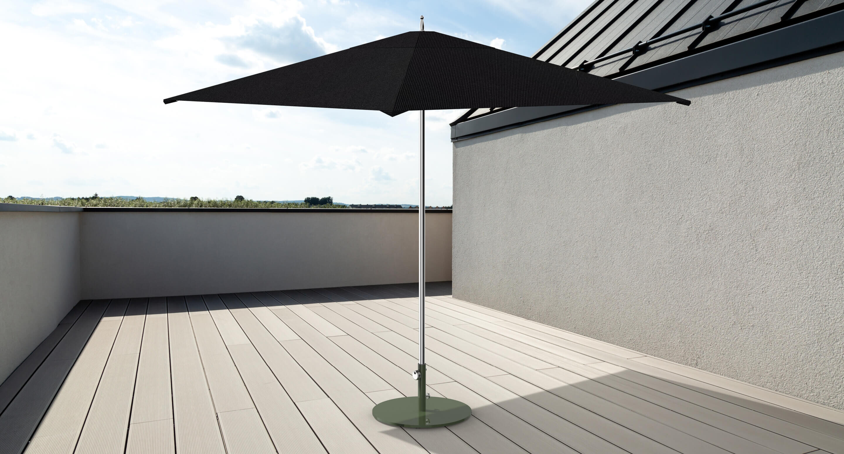 Un parasol noir est posé sur une base circulaire verte sur un toit-terrasse avec un sol en bois clair et des vues partielles du ciel et d'un paysage lointain.