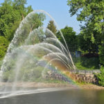 Water spraying with rainbow, trees and riverbank
