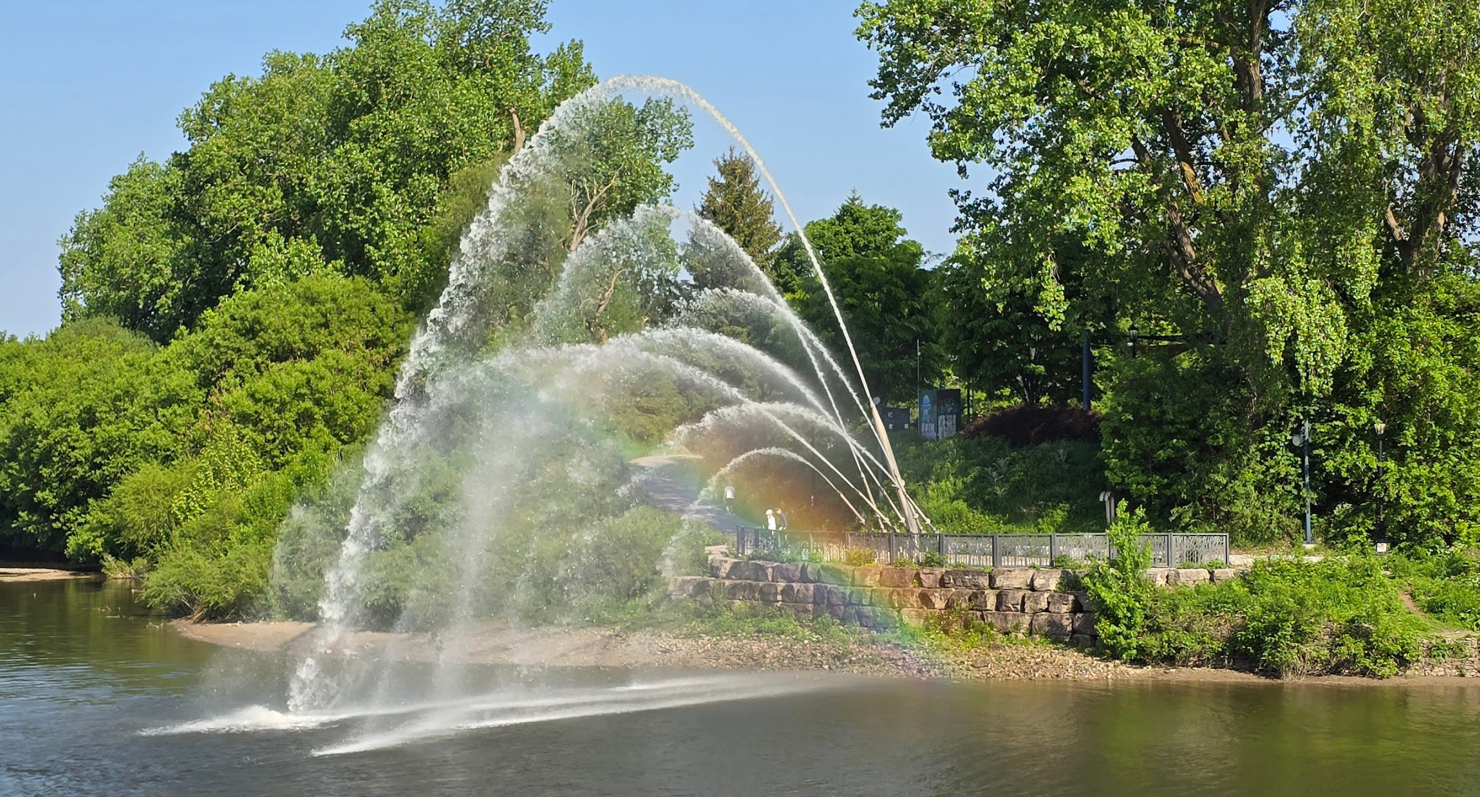 Water spraying with rainbow, trees and riverbank