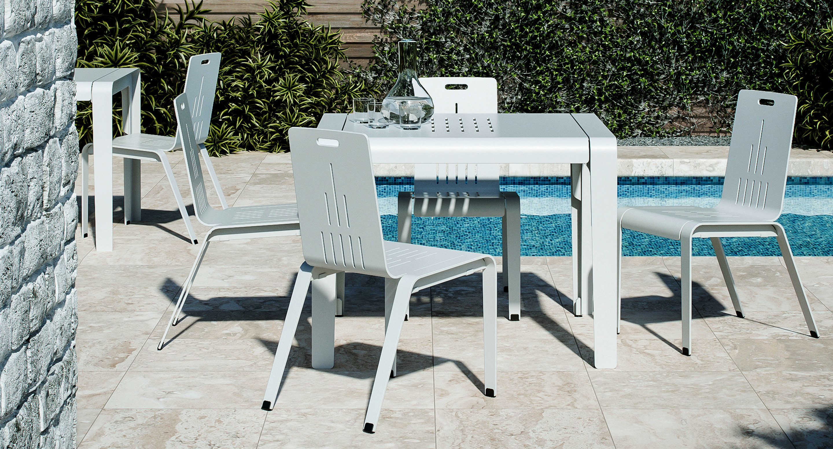 A modern white outdoor table with four matching chairs is set on a tiled patio beside a swimming pool, with plants and a stone wall in the background.