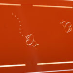 Surface métallique orange avec deux découpes en forme d'abeille et des lignes pointillées, permettant à la lumière de passer à travers le motif.